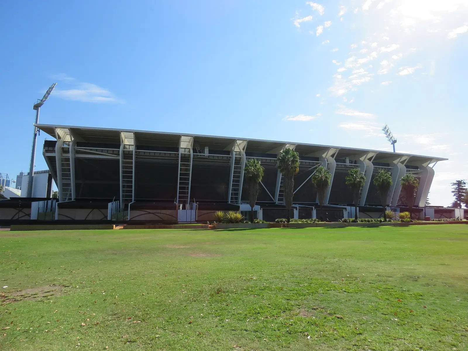 The tiered grandstand of Perth Rectangular Stadium (HBF Park) beside a grass field under blue sky
