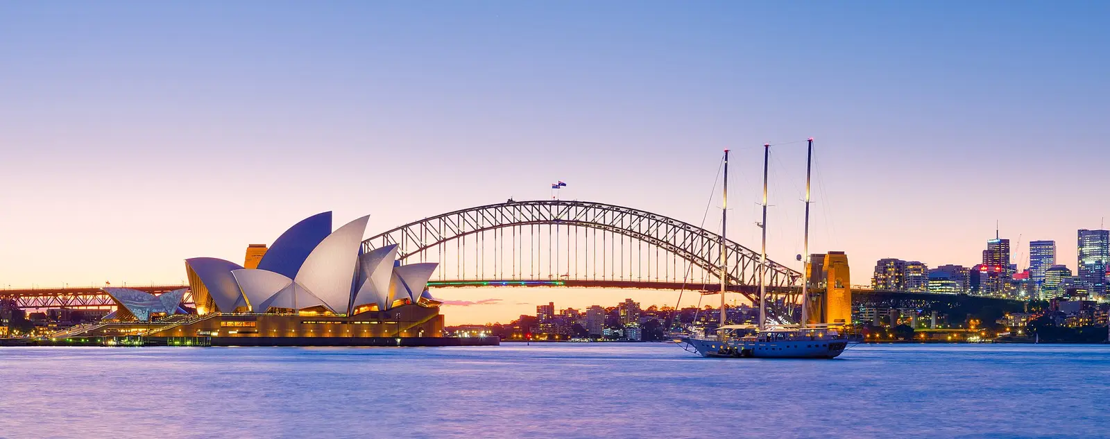 Sydney Opera House and the Harbour Bridge at dusk with the harbour in the foreground